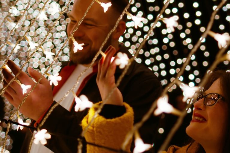 Still from short film Kaleidoscope that is showing at Sit Down Shut Up Festival featuring smiling people surrounded by glowing flower-shaped fairy lights.